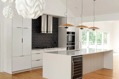 Aiken kitchen with quartz island, cream shaker cabinets with gold hardware, stainless steel range, and veined marble backsplash by Tekton Builds.