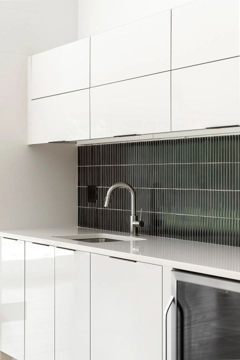 Aiken kitchen with white high-gloss cabinets, dark vertical-stacked tile backsplash, and chrome faucet by Tekton Builds.