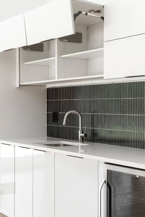 Aiken kitchen with white glossy lift-up cabinets, dark charcoal vertical tile backsplash, and chrome gooseneck faucet by Tekton Builds.