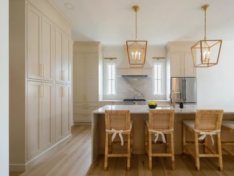 Greenville kitchen with light greige shaker cabinetry, gold hardware, marble island with grey veining, rattan stools, gold pendant lights, and stainless steel range by Tekton Builds.