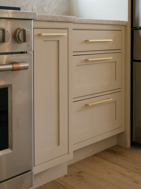 Greenville kitchen detail with light greige shaker cabinets, brass bar pulls, stainless steel range, and marble countertops by Tekton Builds.