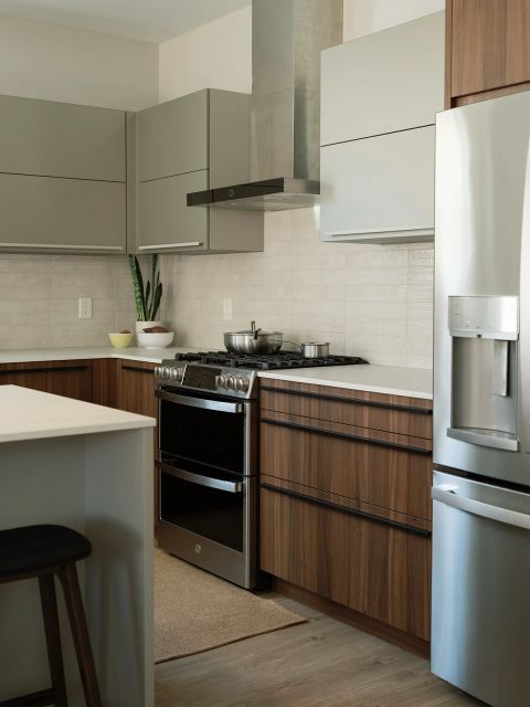 Greenville kitchen with taupe upper cabinets, walnut base cabinets with black pulls, stainless steel double-oven range, textured tile backsplash, and snake plant on white countertop by Tekton Builds.