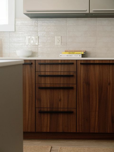 Greenville kitchen with walnut drawer stack, black horizontal pulls, zellige tile backsplash, taupe upper cabinets, and cookbooks on white countertop by Tekton Builds.