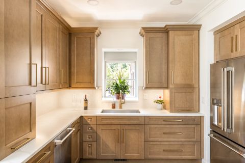 Greenville L-shaped kitchen with light brown wood cabinetry, brushed gold hardware, crown molding, white countertops, gold gooseneck faucet, and stainless steel appliances by Tekton Builds.