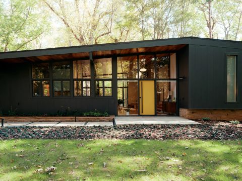 Greenville modern home with dark charcoal paneling, floor-to-ceiling glass, yellow front door, dark sloped roof, and exposed wood soffit by Tekton Builds.