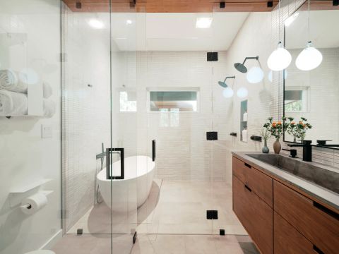 Greenville bathroom with glass-enclosed wet room, freestanding white bathtub, dual matte black rain shower heads, and floating wood vanity by Tekton Builds.