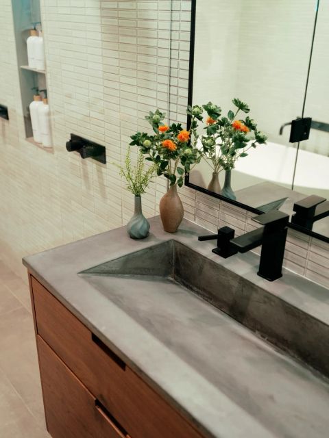 Greenville bathroom with concrete countertop, integrated trough sink, wooden cabinetry, matte black fixtures, and textured tiled accent wall by Tekton Builds.