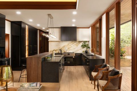 Greenville U-shaped kitchen with dark cabinetry, gold hardware, warm wood waterfall island, and white marble backsplash with gold veining by Tekton Builds.