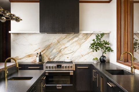 Greenville kitchen with dark wood cabinetry, brass bar pulls, black speckled countertops, marble backsplash with gold veining, and brass chandelier by Tekton Builds.