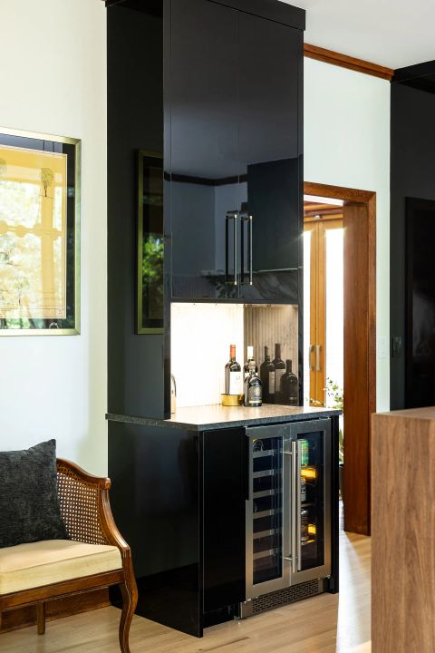 Greenville custom home bar with glossy black lacquered cabinet, brushed gold pull handles, wine bottles, and dual-zone wine cooler by Tekton Builds.