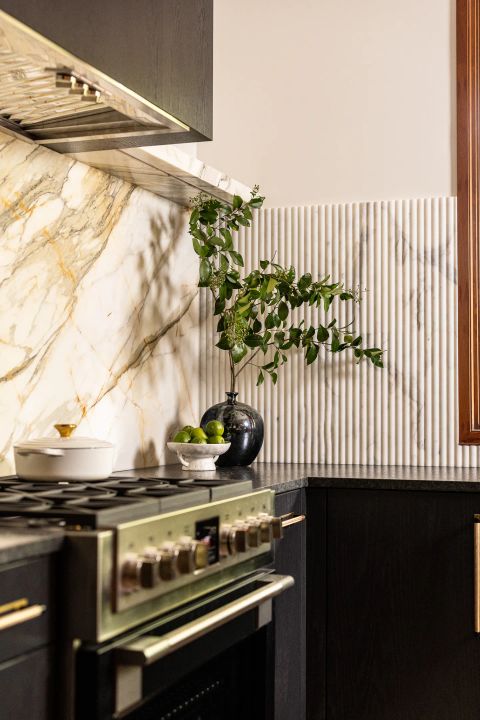 Greenville kitchen with stainless steel range, brass accents, dark espresso-stained wood cabinetry, and white marble backsplash with grey and golden-brown veining by Tekton Builds.
