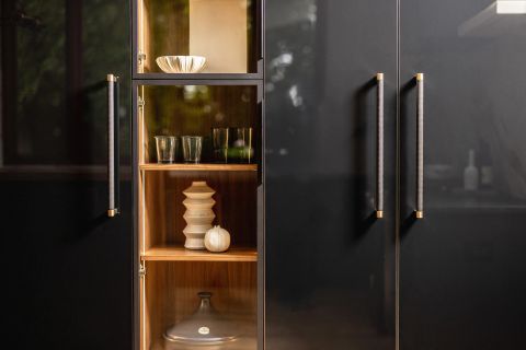 Greenville kitchen cabinetry with dark grey cabinet doors, long vertical brass pull handles, warm-toned wood open shelving, and LED lighting by Tekton Builds.