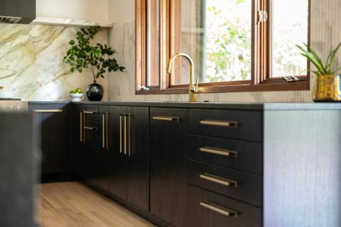 Greenville kitchen with dark espresso-stained wood base cabinets, brass hardware, dark matte countertop, golden gooseneck faucet, and white marble backsplash by Tekton Builds.