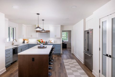 Taylors kitchen with two-tone cabinetry, central island with brown base and white countertop, black bar stools, and black and gold pendant lights by Tekton Builds.